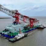 Navio de cravação de estacas Tie Jian Da Qiao Zhuang 1, com guindaste vermelho e branco, rebocado por embarcações de apoio ao deixar o Porto de Lüsi, na China