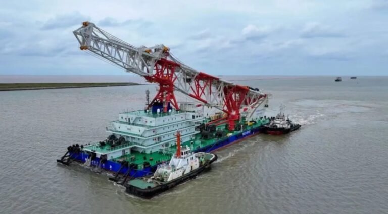 Navio de cravação de estacas Tie Jian Da Qiao Zhuang 1, com guindaste vermelho e branco, rebocado por embarcações de apoio ao deixar o Porto de Lüsi, na China