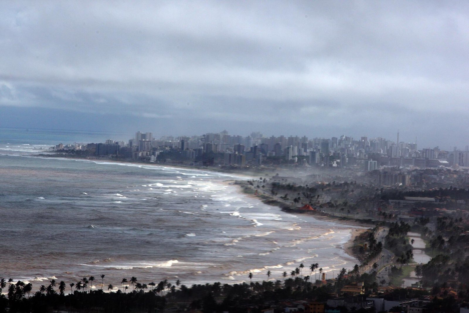 Vista aérea da orla de Salvador com mar agitado e céu carregado de nuvens de chuva