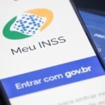 Tela do aplicativo Meu INSS em um celular, ao lado de cartão da Previdência Social.