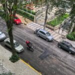 Motociclista de capacete trafega entre carros estacionados em rua, vista de cima
